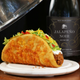 Taco Bell Chalupa on white plate atop wooden table with bottle of Taco Bell Jalapeno Noir on the side